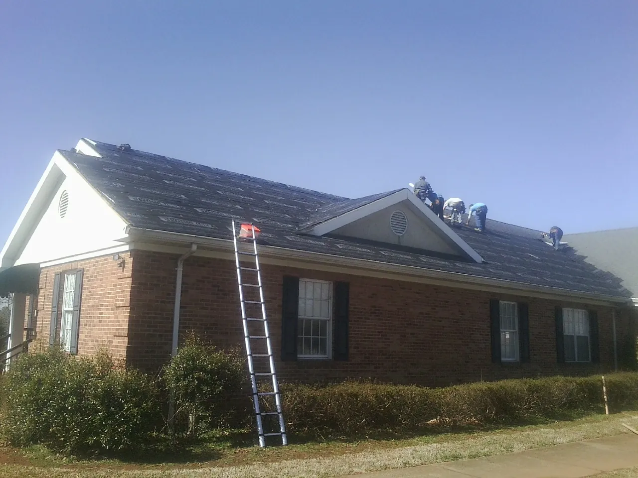 Crew tearing shingles off a brick ranch roof with a ladder set — Emergency Roof Repair work by our crew in Gratz