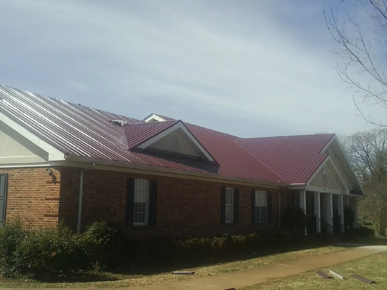 Red metal roof with gabled entries on a long brick building, from a Hail Damage Roof Repair job in Gratz