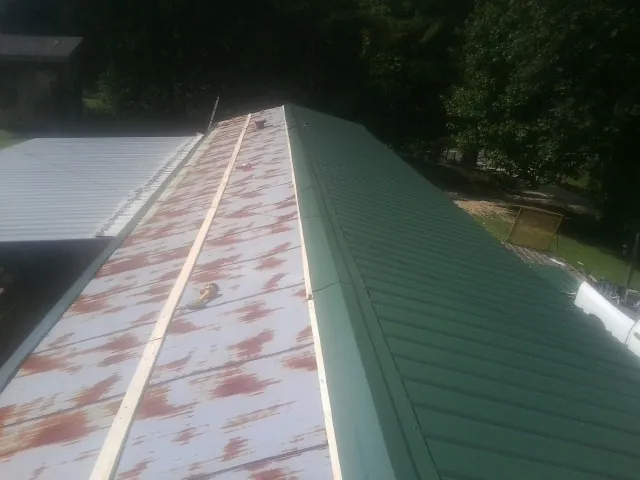 Old rusted panels beside newly installed green metal roofing — Wind Damage Roof Repair by Roofing Brothers in Gratz