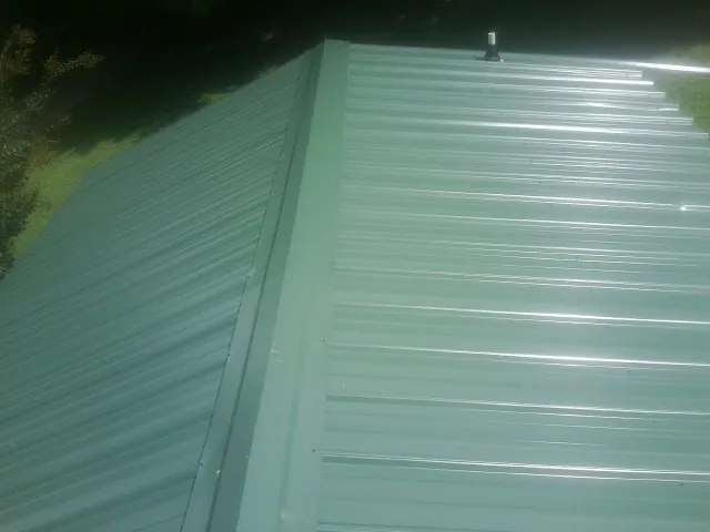 New green metal panels meeting at the ridge of a roof — Flat Roof Repair work by our crew in Gratz