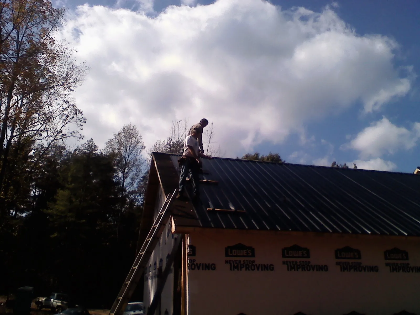 Roofer fastening dark metal panels high against a cloudy sky, from a Roof Inspection job in Gratz