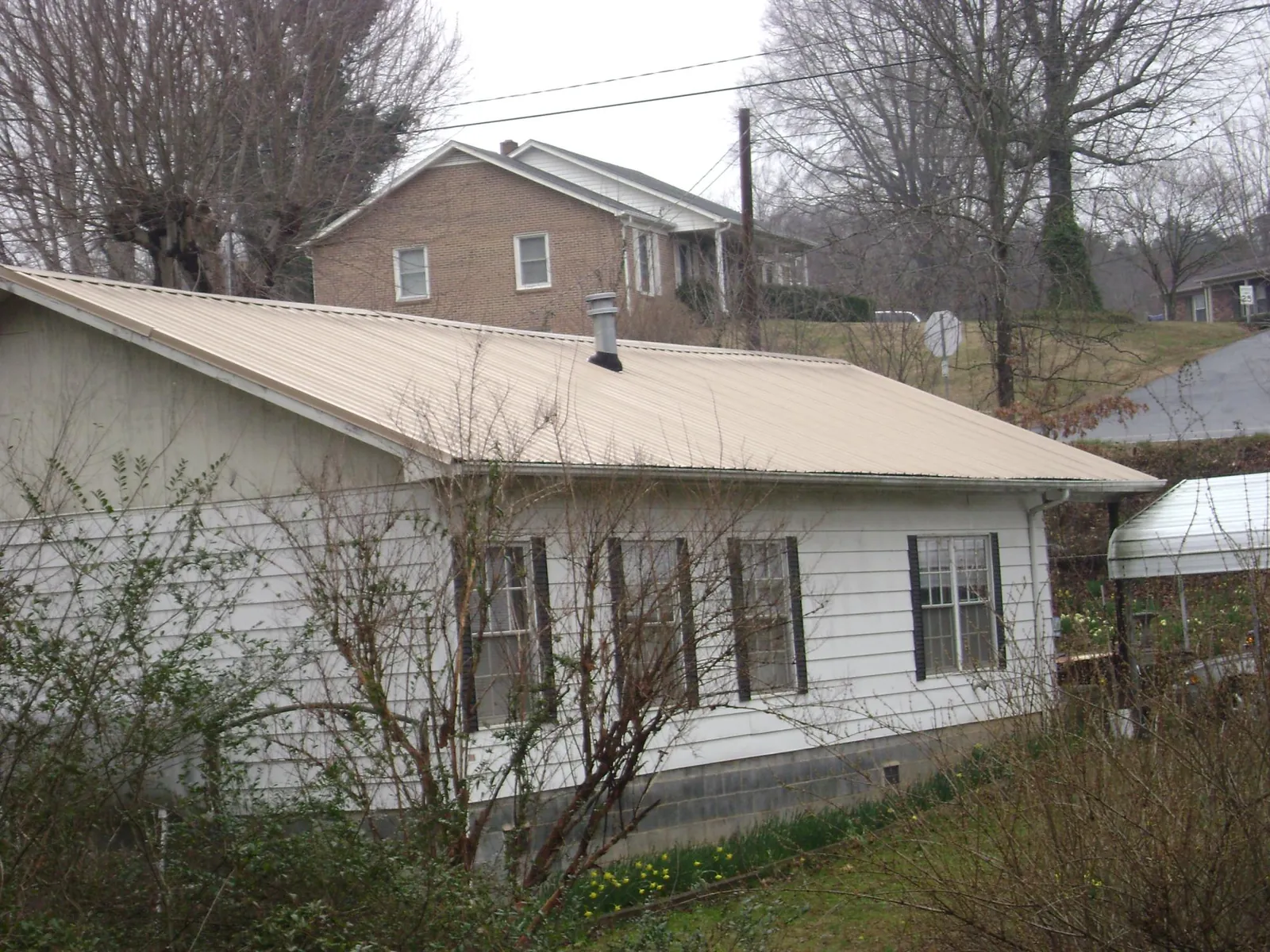 Tan metal roof on a white sided house set into a hillside — Commercial Roofing by Roofing Brothers in Gratz
