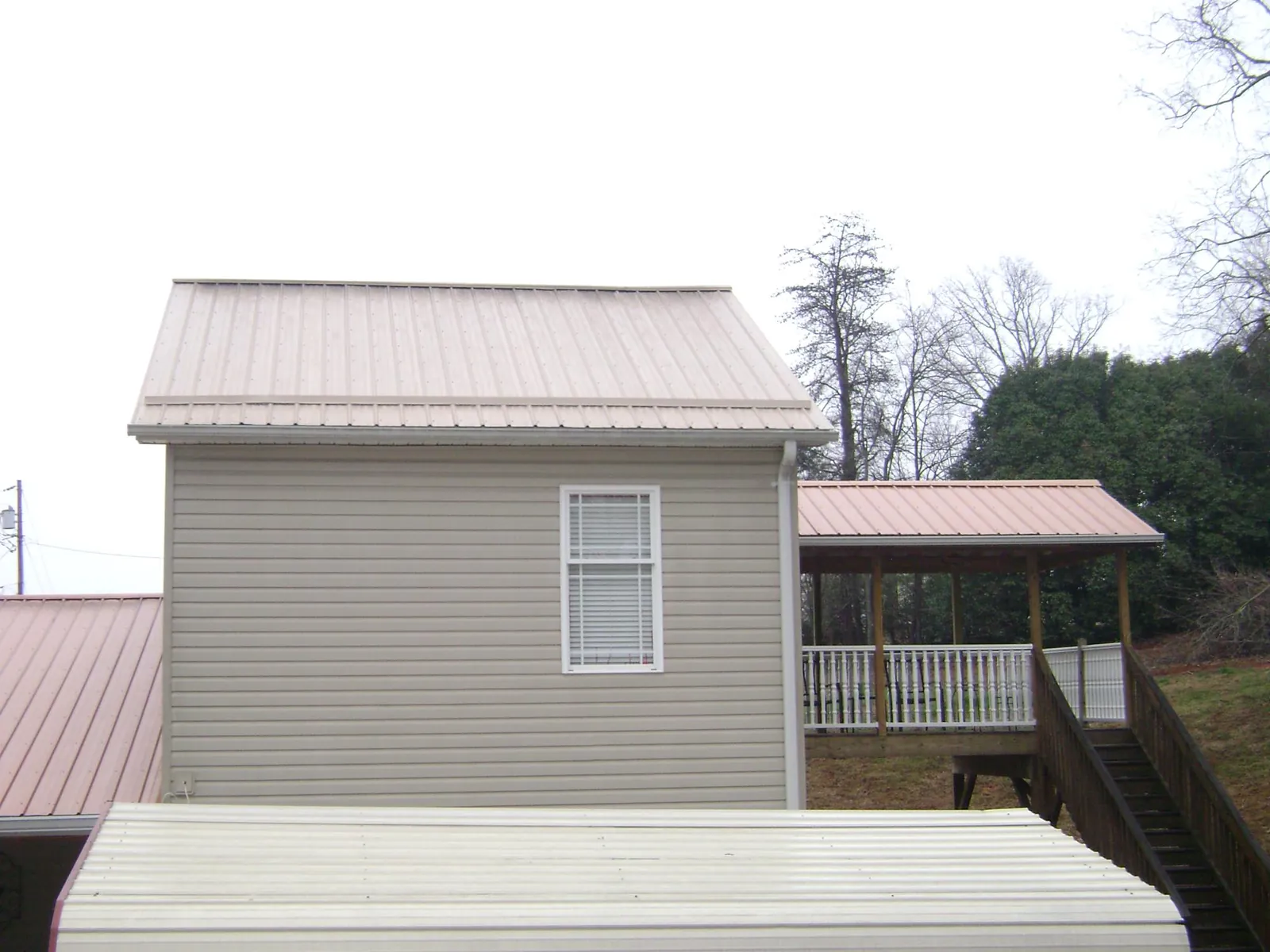 Tan metal roofs on a two story addition and attached porch, from a Roof Replacement job in Gratz